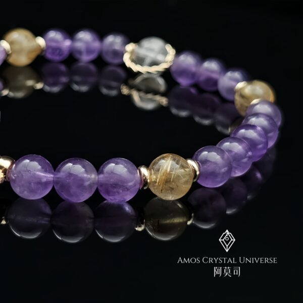 「紫韻金靈」水晶手鍊實拍照，展現紫水晶主石搭配金鈦晶與藍針水晶的細緻設計，圓珠晶礦細膩柔美，象徵靈性、智慧與四方來財能量，襯托女性優雅氣質與自然之美。